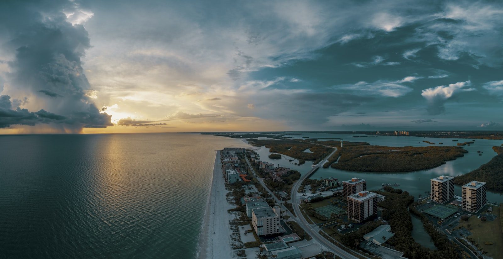 Aerial view of Florida's Gulf Coast at sunset, storm clouds over turquoise water and a barrier-island shoreline