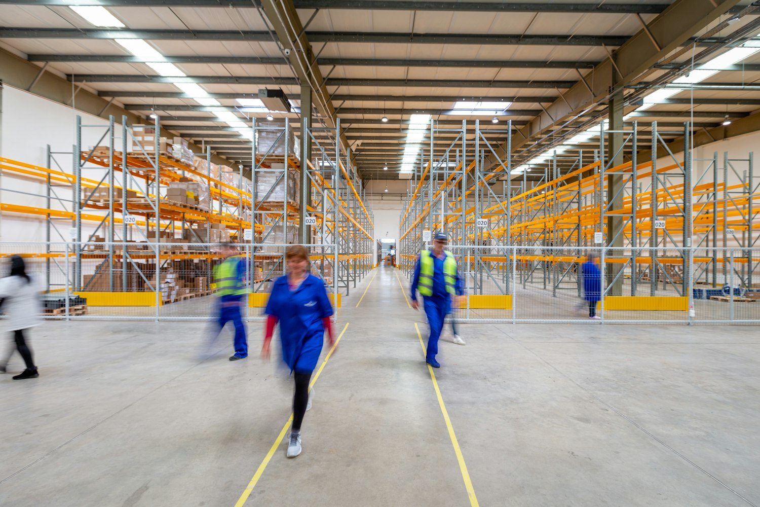 Interior of a large warehouse with tall orange steel pallet racking and crew members working on the floor